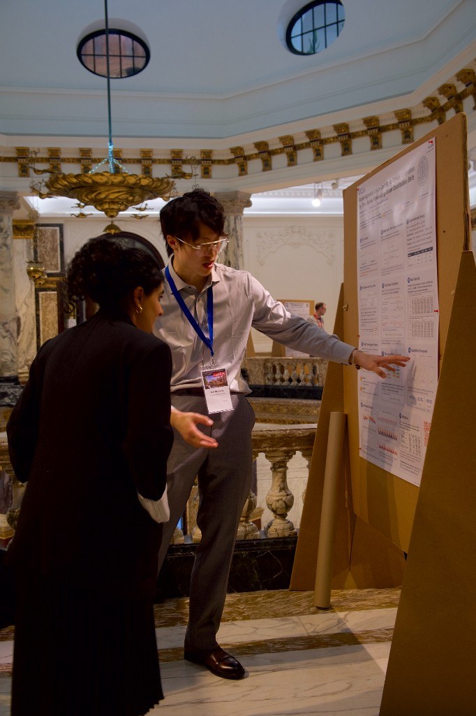 Presenting the OMPB poster to an attendee in the Marble Hall at UAI 2026
